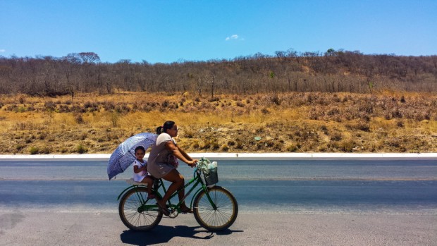 Mulher anda de v=bicicleta com seu filho, na BR 365, ao fundo  vegetação de Caatinga. ( Foto Joel Silva / Folhapress)